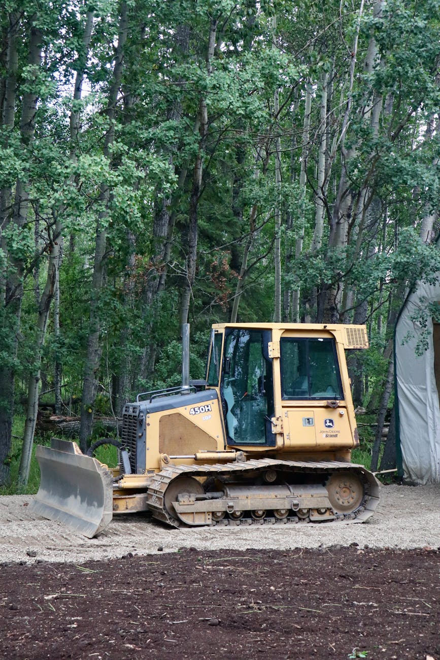 Yellow bulldozer in forest clearing preparing soil for landscaping project.