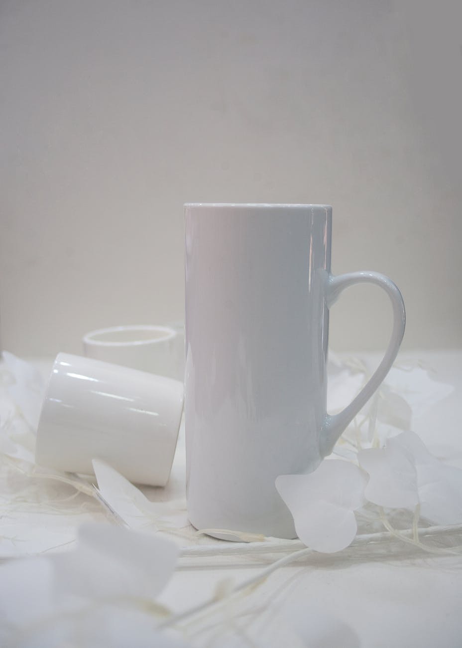 Elegant white ceramic mugs surrounded by delicate white petals on a clean background.