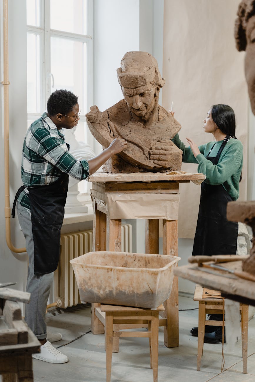 Two artists collaborate on a clay sculpture, shaping a new artwork in a creative workshop.