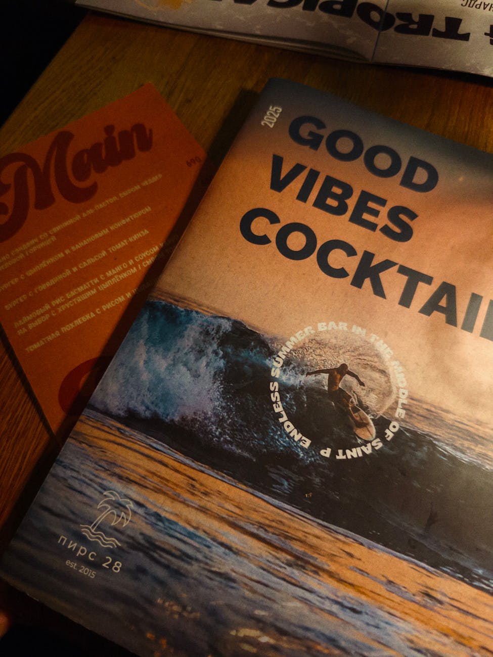 A cocktail magazine featuring a surfer on a wave, lying on a wooden table.