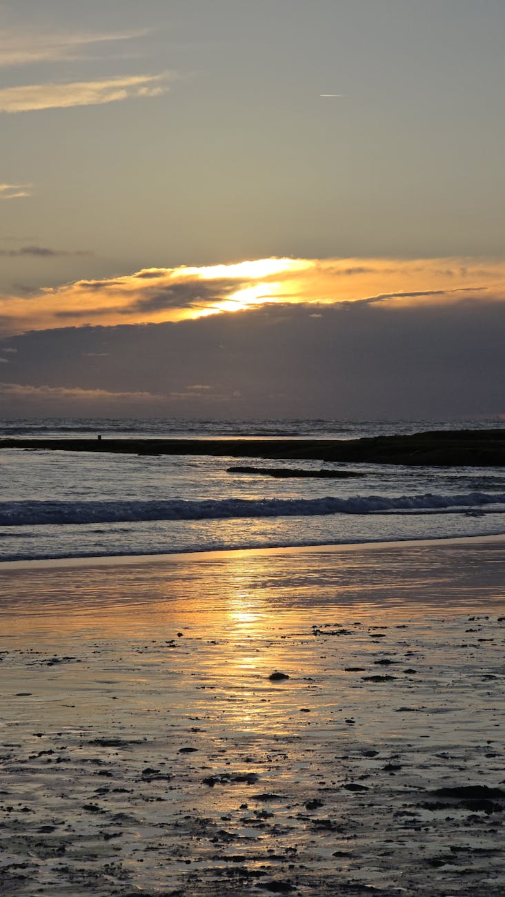 Peaceful sunset over an ocean beach with reflections on wet sand, perfect for relaxing scenery.