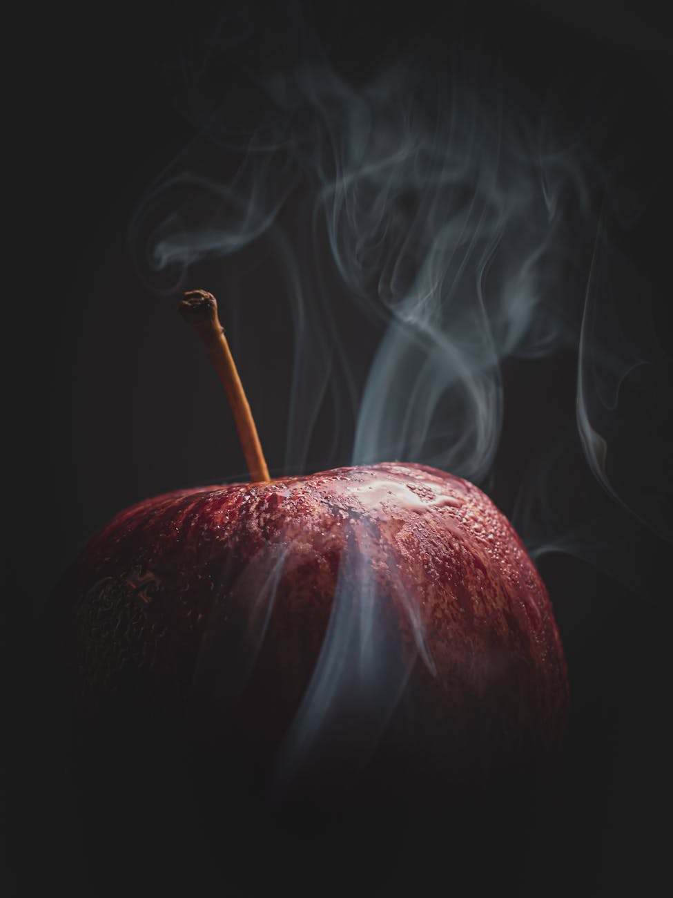 Artistic close-up of a red apple with smoke on a black background, creating a mysterious mood.